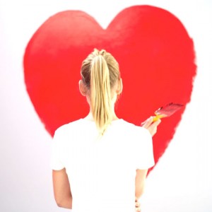 young woman painting a red heart on the wall